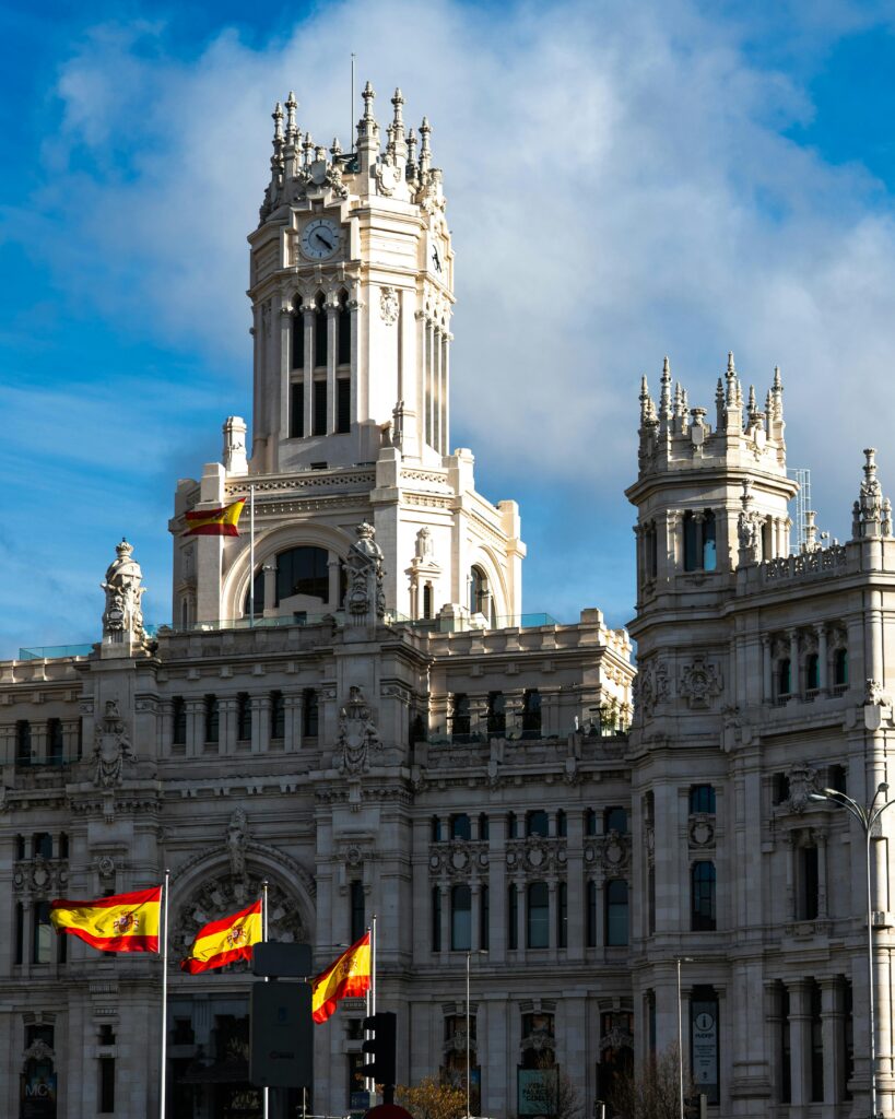 pexels-photo-30732161-30732161 The iconic Palacio de Cibeles in Madrid with Spanish flags waving under a blue sky.