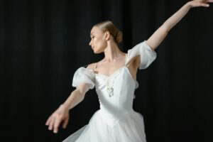 Graceful ballerina in white tutu performing dance on stage against a black backdrop.