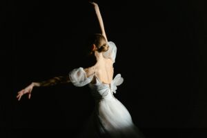 Graceful back view of a ballerina dancing on stage with dramatic lighting.